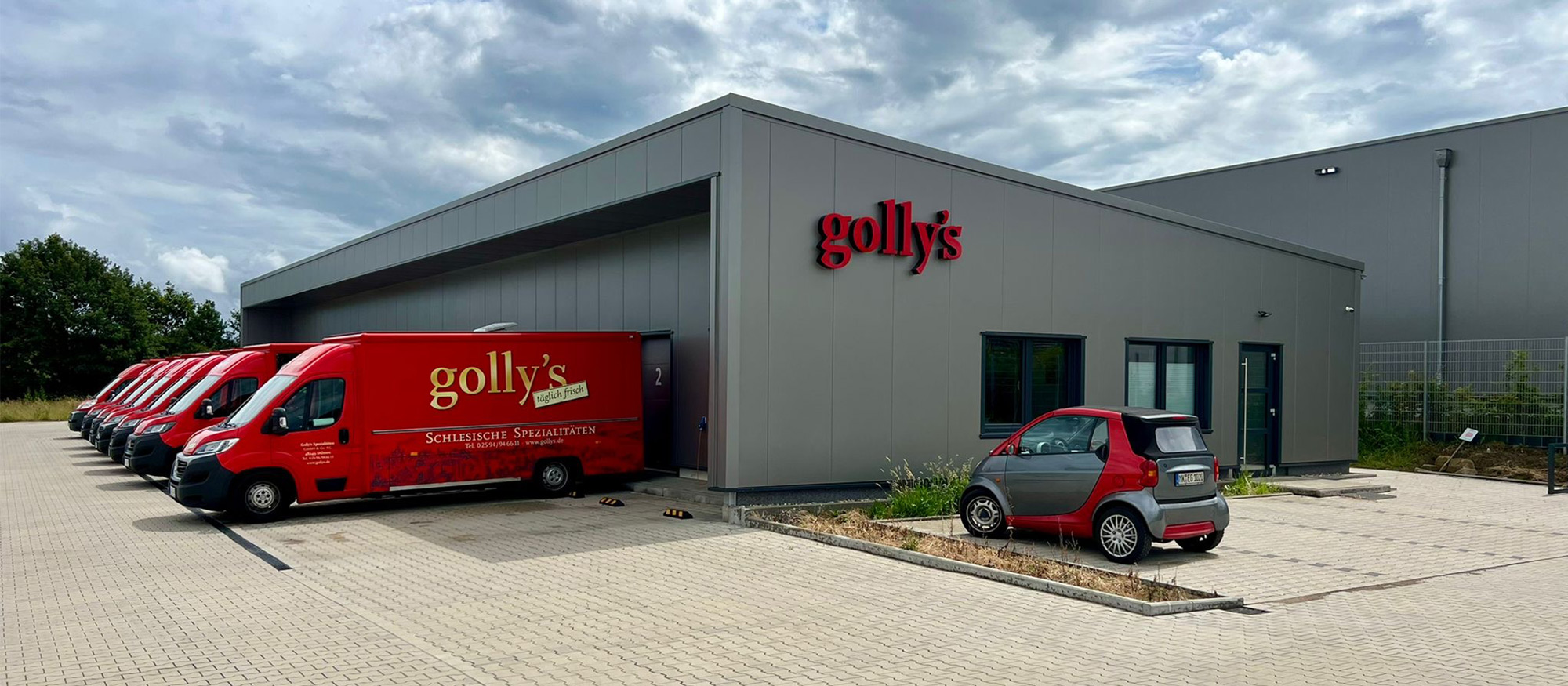 Frontalansicht einer großen grauen Pultdachhalle der Firma golly's